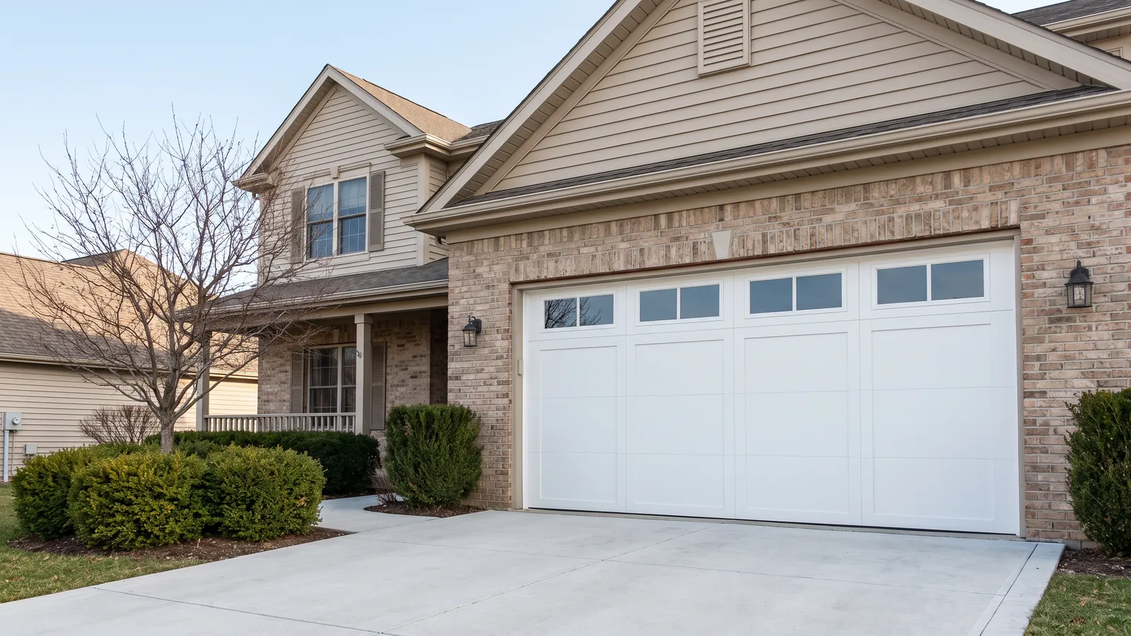 Newly installed white insulated steel carriage-style garage door with a row of square windows on a two-story suburban home with a brick front in Johnson County, Kansas